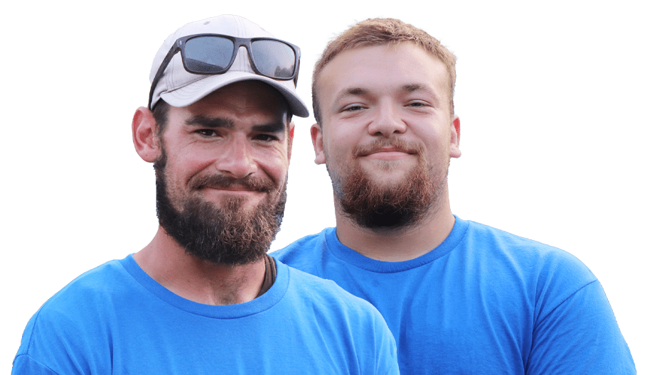 Two men wearing blue shirts and sporting beards are smiling at the camera. The man on the left, possibly Davis from Davis Painting, is wearing a cap with sunglasses perched on top, and the man on the right has short hair. Both appear to be outdoors given the bright natural light.