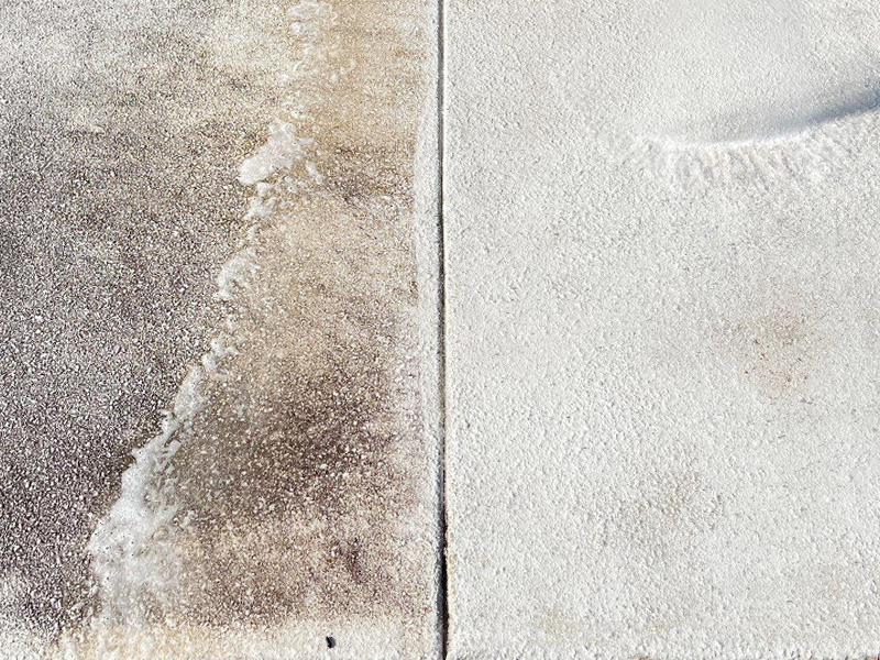 A concrete surface divided in half; the left side is dirty and stained, while the right side—treated by SUDS Power Washing—is clean and white, showing a striking contrast between the two sections.